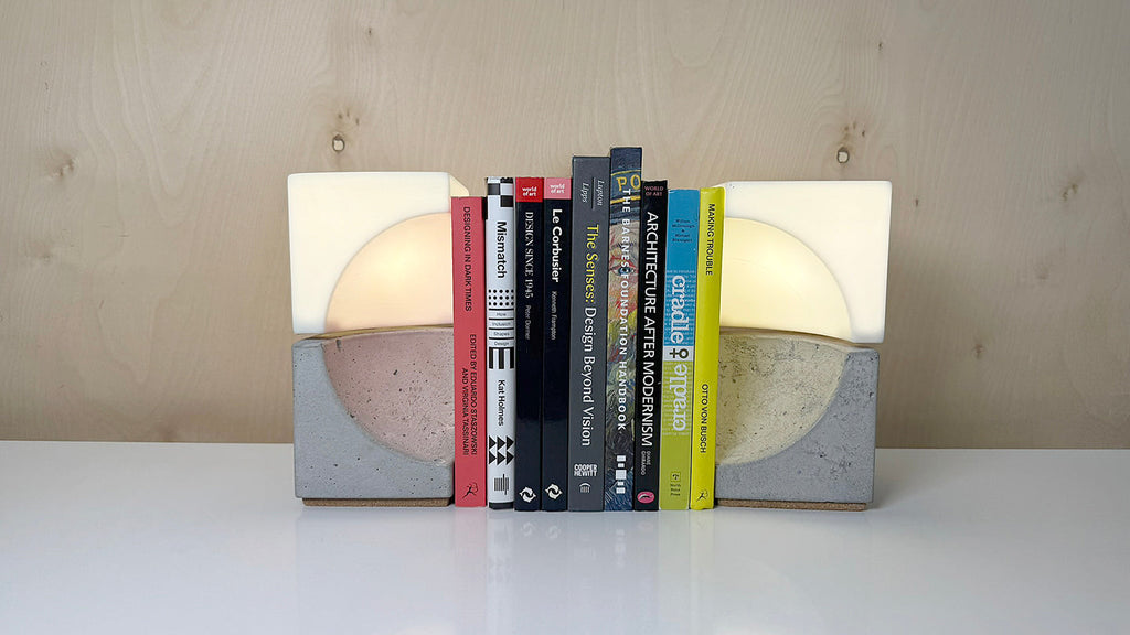 Two concrete bookends with white light tops holding up 9 books on a white tabletop