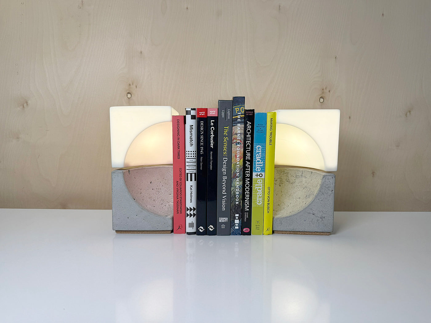 Two concrete bookends with white light tops holding up 9 books on a white tabletop