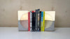 Two concrete bookends with white light tops holding up 9 books on a white tabletop